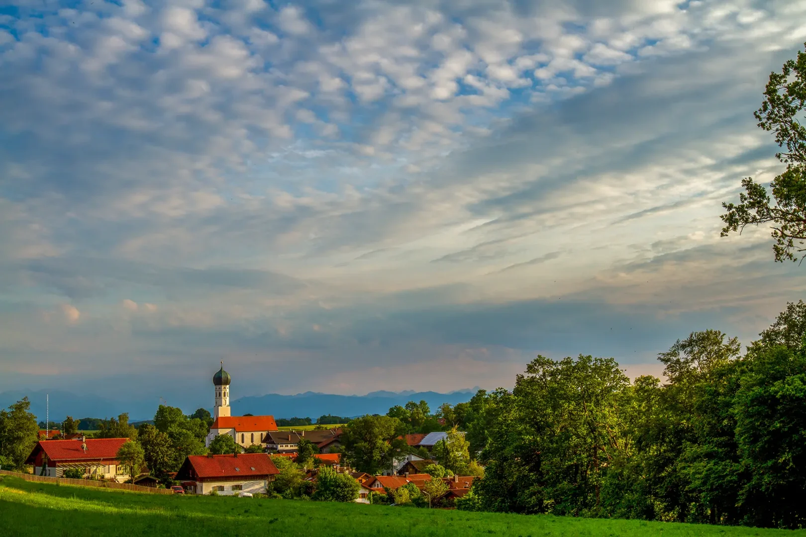 Die Gemeinde Münsing erstreckt sich über die sanften, eiszeitlich geprägten Hügelketten des Ostufers. Von den Höhenstraßen aus eröffnen sich immer wieder Postkarten-Panoramen: Im Vordergrund das tiefe Blau des Sees, dahinter das saftige Grün der Wiesen und am Horizont die mächtige, weiße Kette der Alpen.