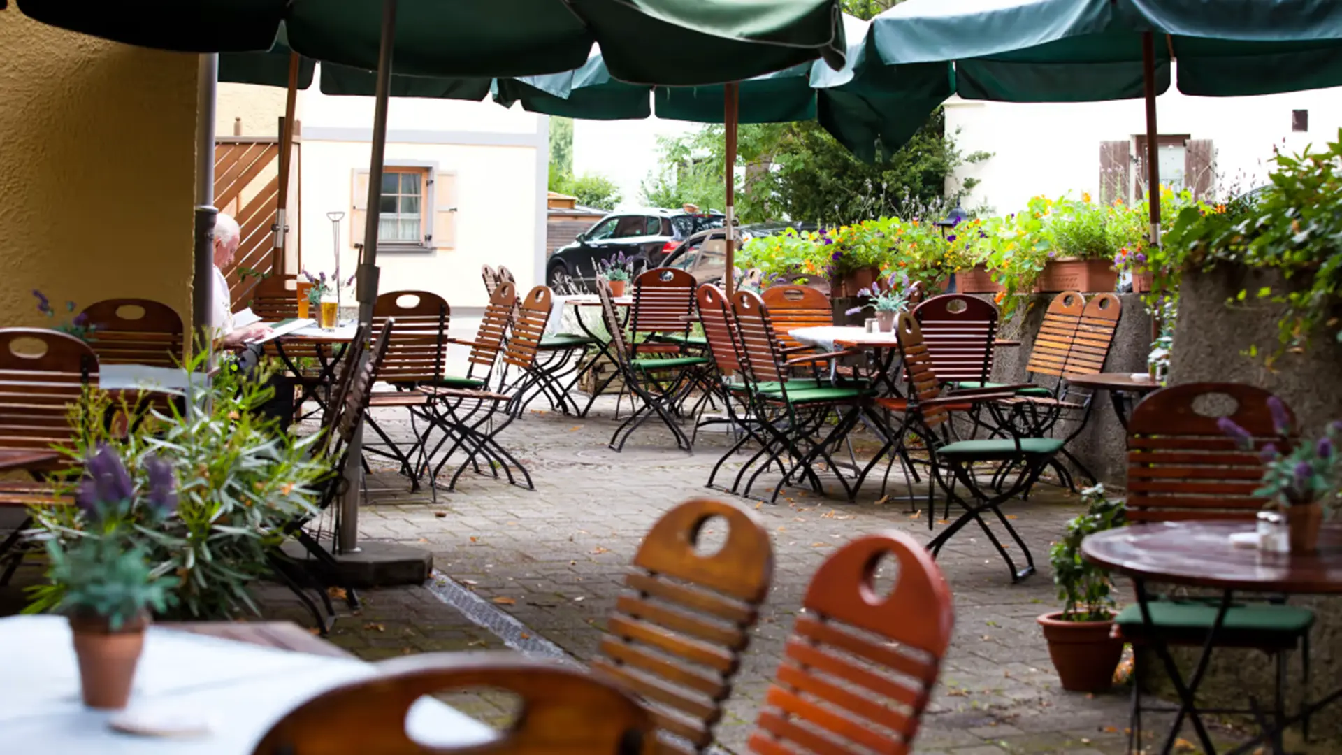 Biergarten des Posthotels Pöcking mit Klappstühlen unter grünen Schirmen