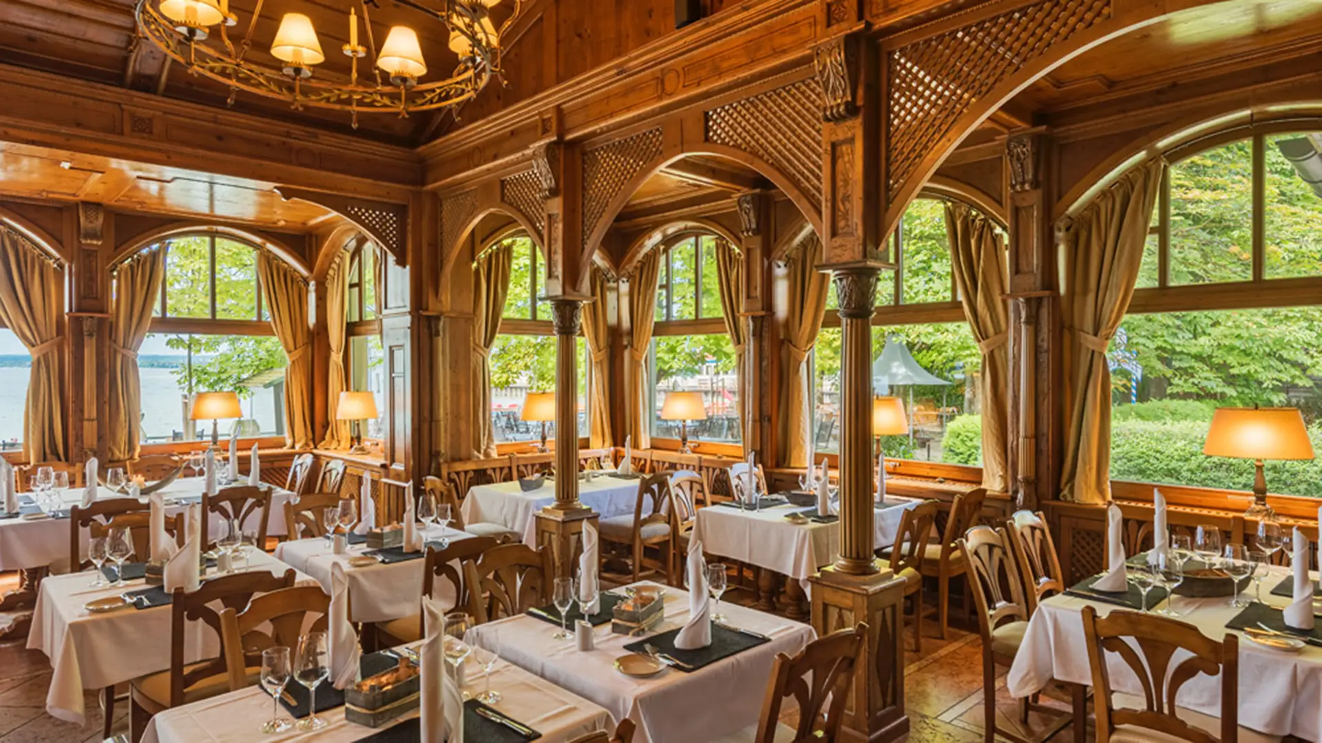 Panoramasaal im Seehaus Schreyegg am Ammersee mit geschnitzten Holzsäulen, Rundbogenfenstern und Blick auf den See