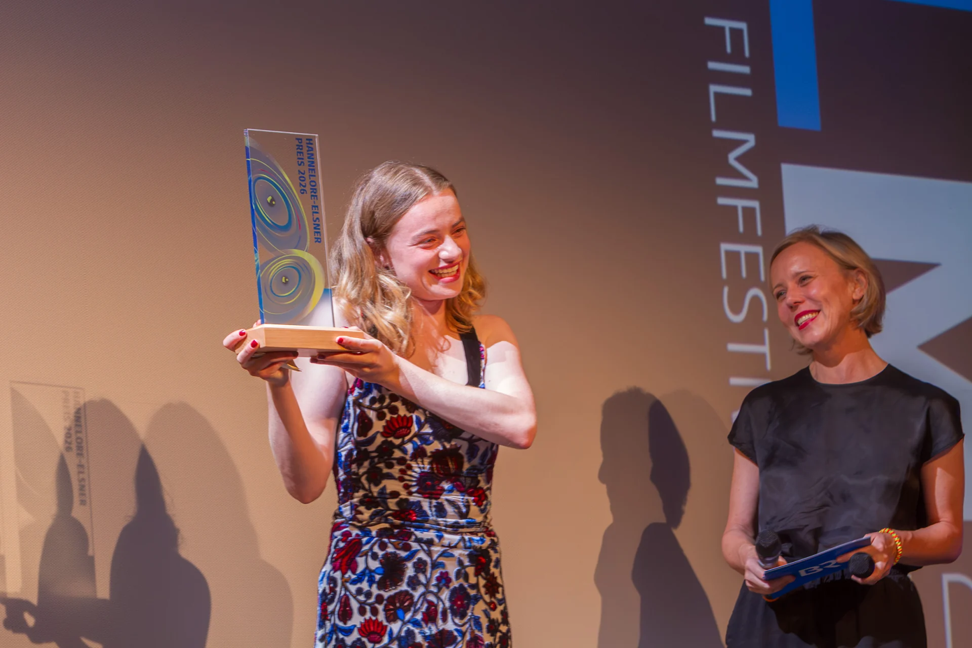 Luna Wedler hält die Trophäe des Hannelore-Elsner-Preises 2026 hoch, rechts Moderatorin Christina Wolf, auf der Bühne der Schlossberghalle Starnberg
