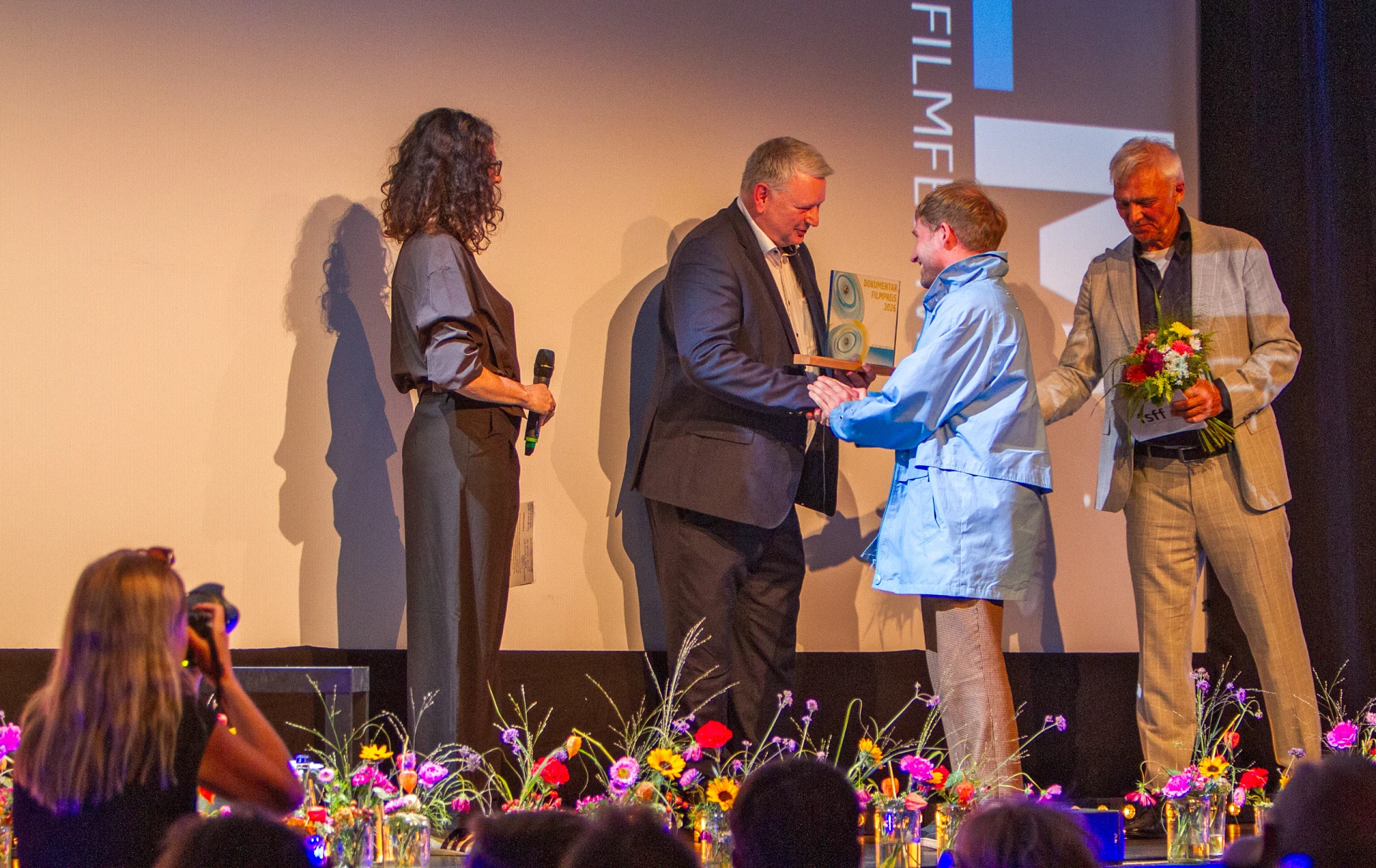 Rupert Berghofer überreicht Jonas Spriestersbach die gläserne Trophäe des Dokumentarfilmpreises 2026 in der Schlossberghalle Starnberg