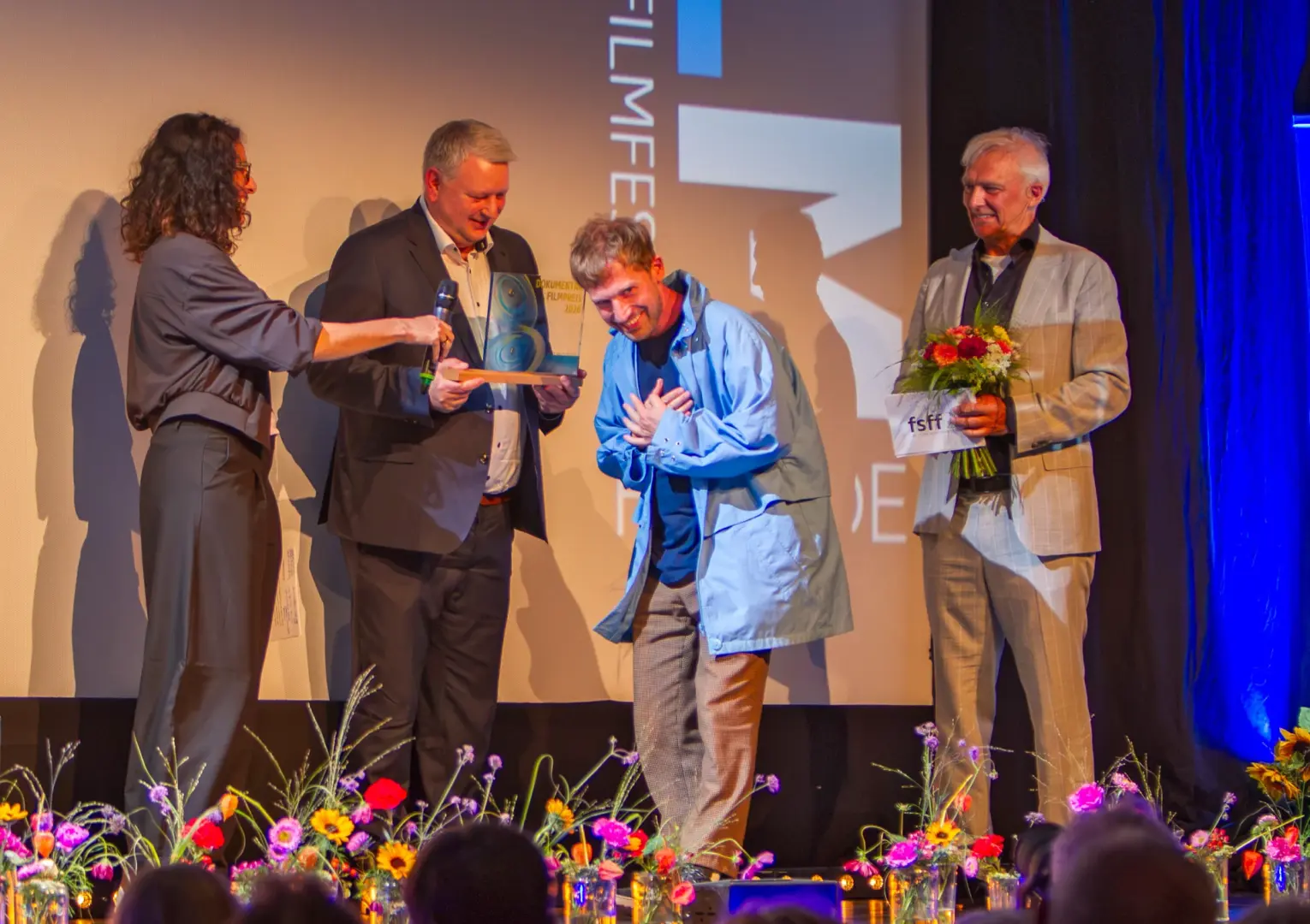 Jonas Spriestersbach verneigt sich mit der Hand auf der Brust auf der Bühne der Schlossberghalle Starnberg, daneben Maja Reichert, Rupert Berghofer und Matthias Helwig