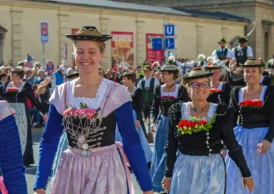 Junge Frauen in Dirndln mit Spitzenmiedern und Blumenschmuck laufen lachend in einer Trachtengruppe, Trachten- und Schützenzug München
