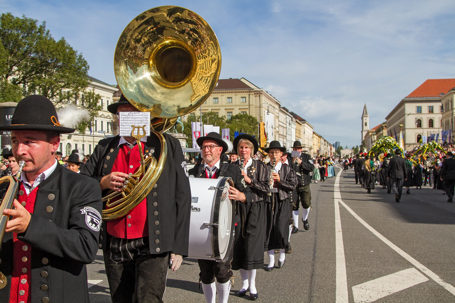 Ein Tubaspieler und Musiker in schwarzen Uniformen mit roten Westen marschieren die Ludwigstraße hinauf, im Hintergrund die Ludwigskirche, Trachten- und Schützenzug München