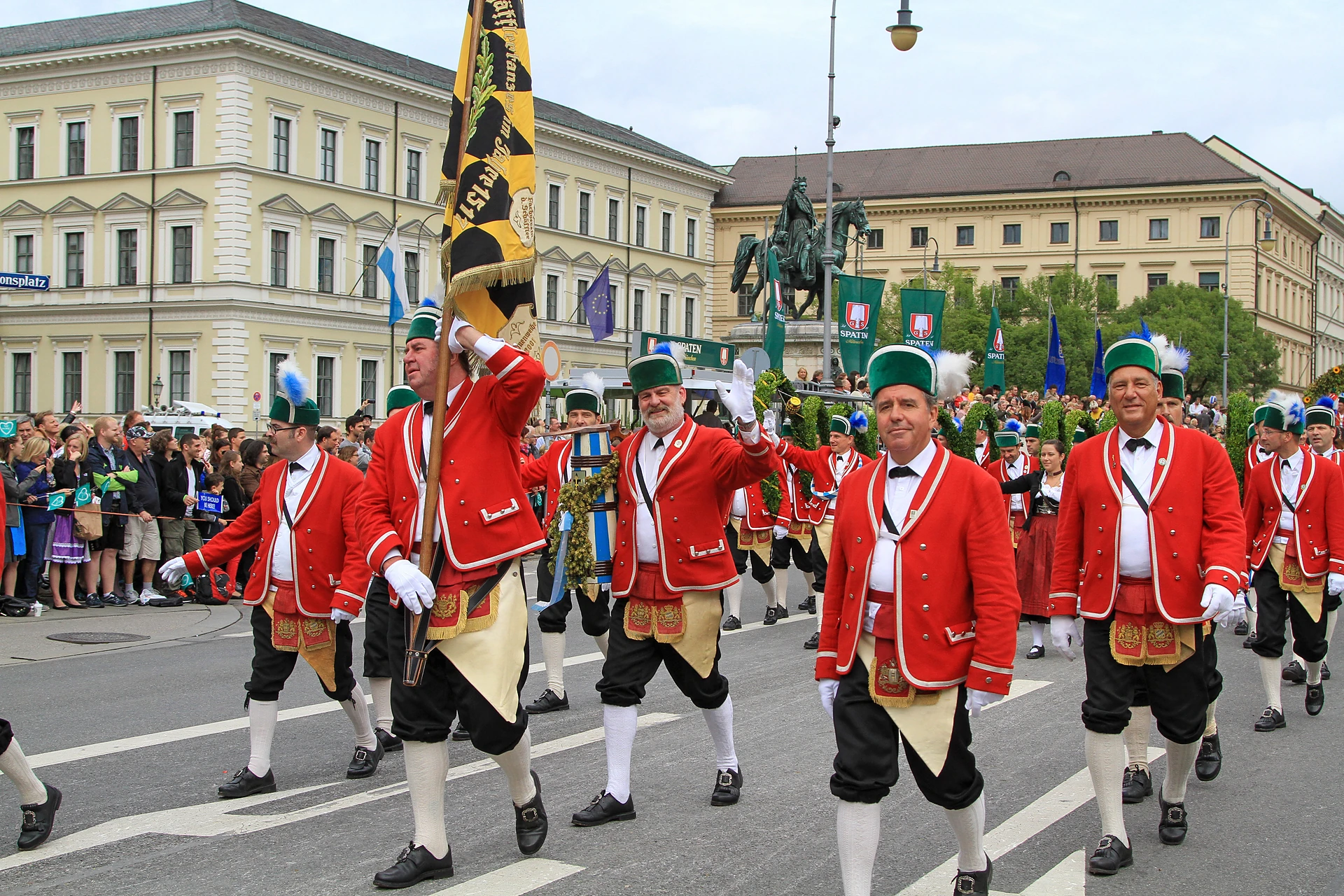 Schäffler in roten Röcken und grünen Kappen marschieren mit ihrer Fahne über den Odeonsplatz beim Trachten- und Schützenzug in München