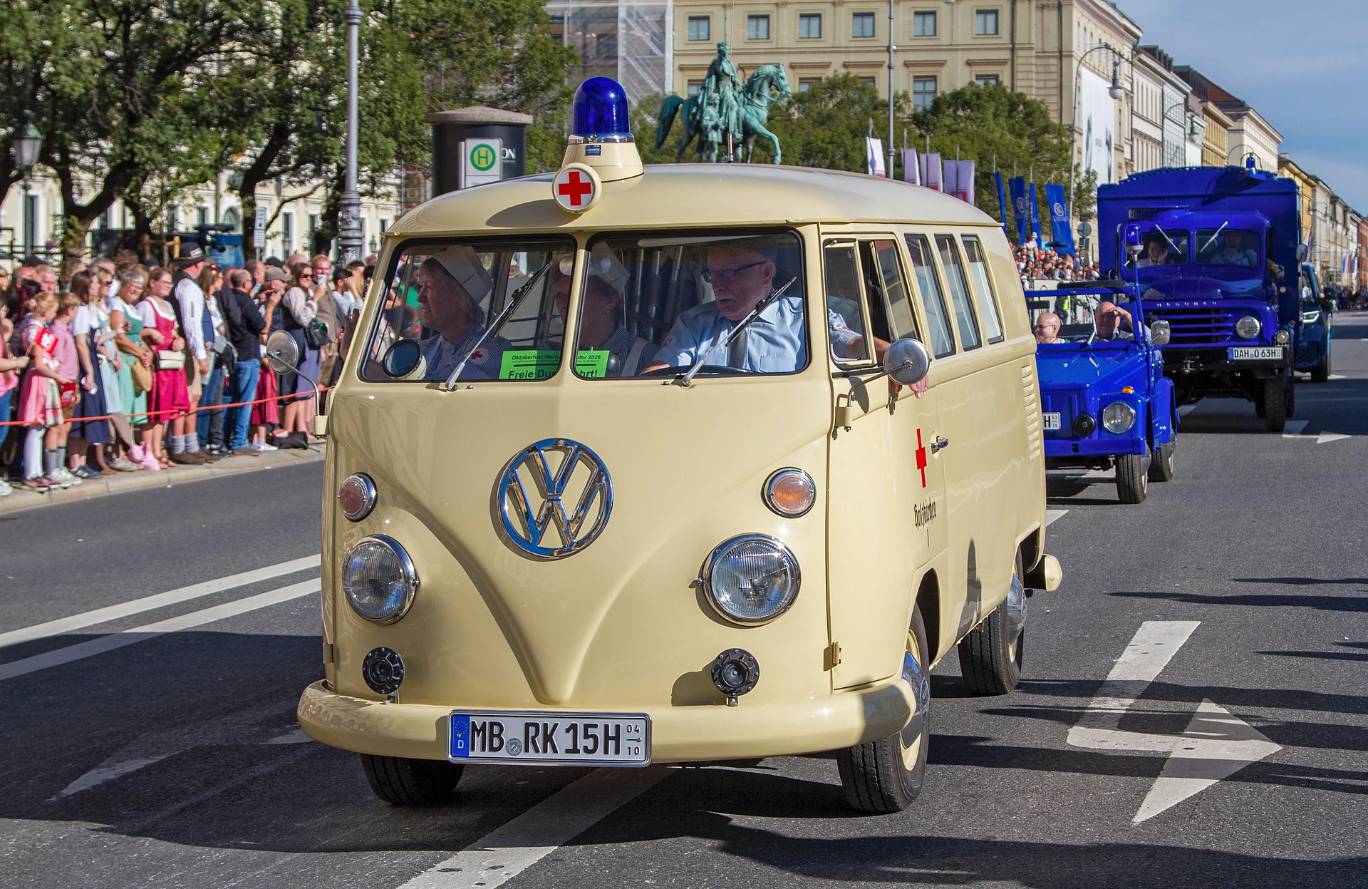 Ein historischer VW-Bus des Roten Kreuzes mit Blaulicht und rotem Kreuz fährt beim Trachten- und Schützenzug über die Ludwigstraße, im Fahrzeug Männer in grauen Uniformen und Frauen in historischer Schwesterntracht, München