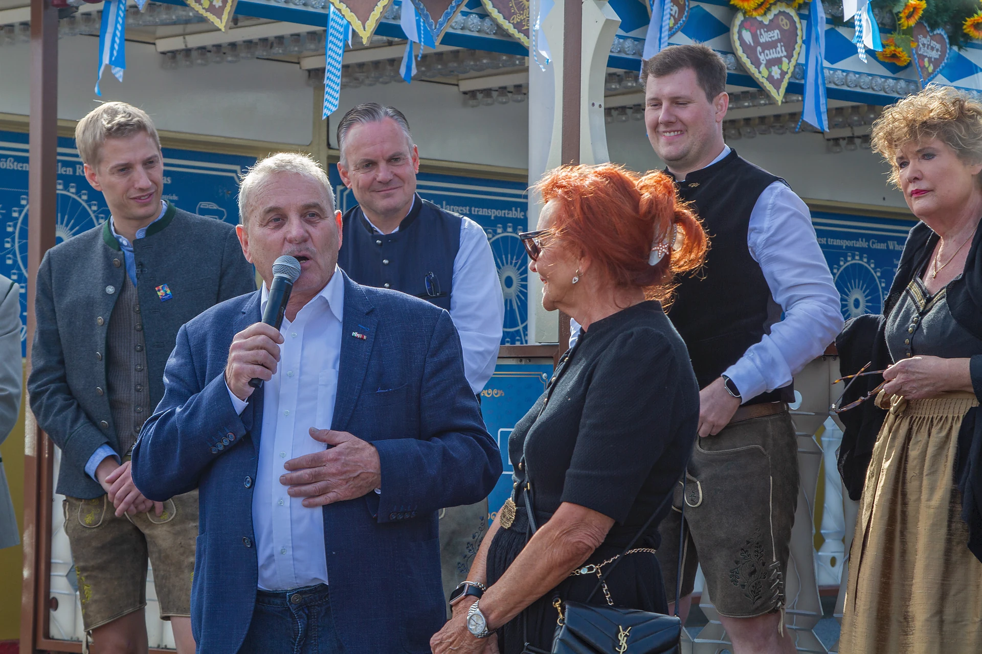 Albert Ritter vom Deutschen Schaustellerbund spricht ins Mikrofon vor dem Riesenrad, daneben Oberbürgermeister Dominik Krause, Wiesnchef Christian Scharpf und Margit Ramus, Oktoberfest München. PersonInImage: Dominik Krause, Albert Ritter, Christian Scharpf, Margit Ramus