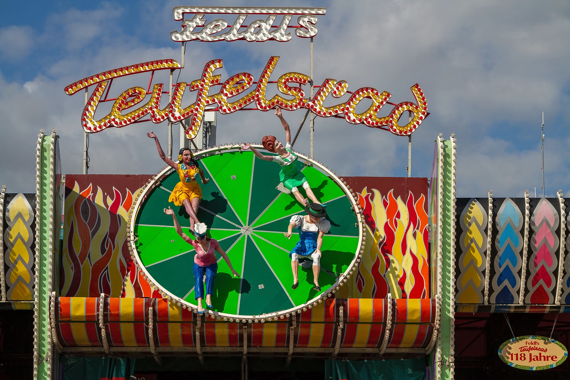 Bemalte Figuren auf dem grünen Rad über dem Eingang von Feldl's Teufelsrad mit Leuchtschrift, Oktoberfest München