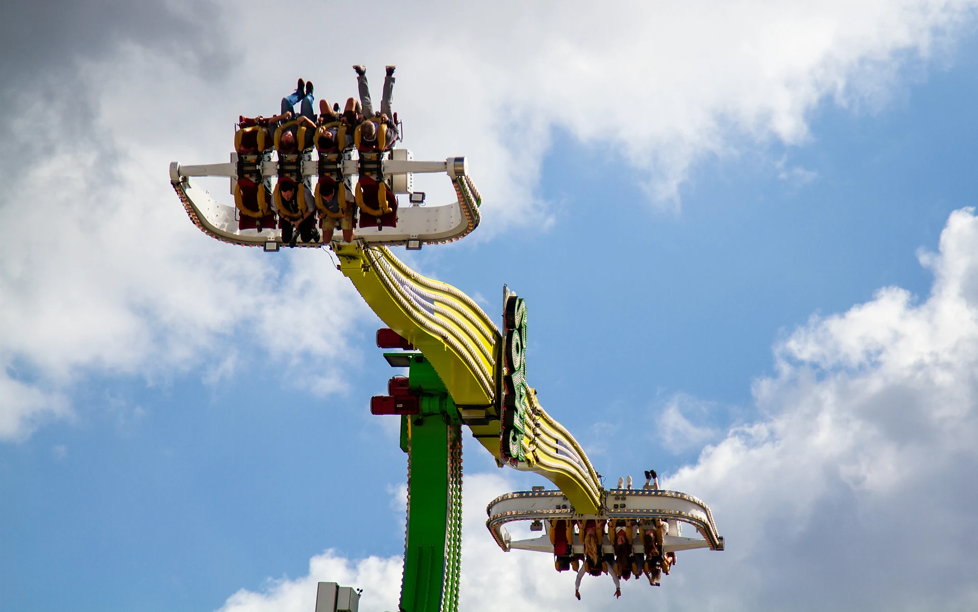 Zwei Gondelreihen des Fahrgeschäfts Chaos Pendel mit Fahrgästen überschlagen sich hoch über dem Boden vor bewölktem Himmel, Oktoberfest München