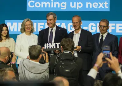 Sechs Personen stehen nebeneinander auf einer Bühne und halten ein Schild mit der Aufschrift Hashtag M T M, davor eine Reihe fotografierender Journalisten.