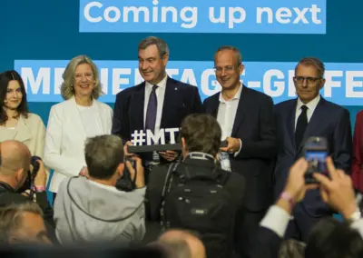 Gruppenfotoaufnahme -stehend auf der Bühne Eva Schulz, Dr. Katja Wildermuth, Dr. Markus Söder, Dr. Thorsten Schmiege, Marco Giordani und Prof. Dr. Alexandra Borchardt - davor Fotoreporter und das Schild #MT in Söders Hand.