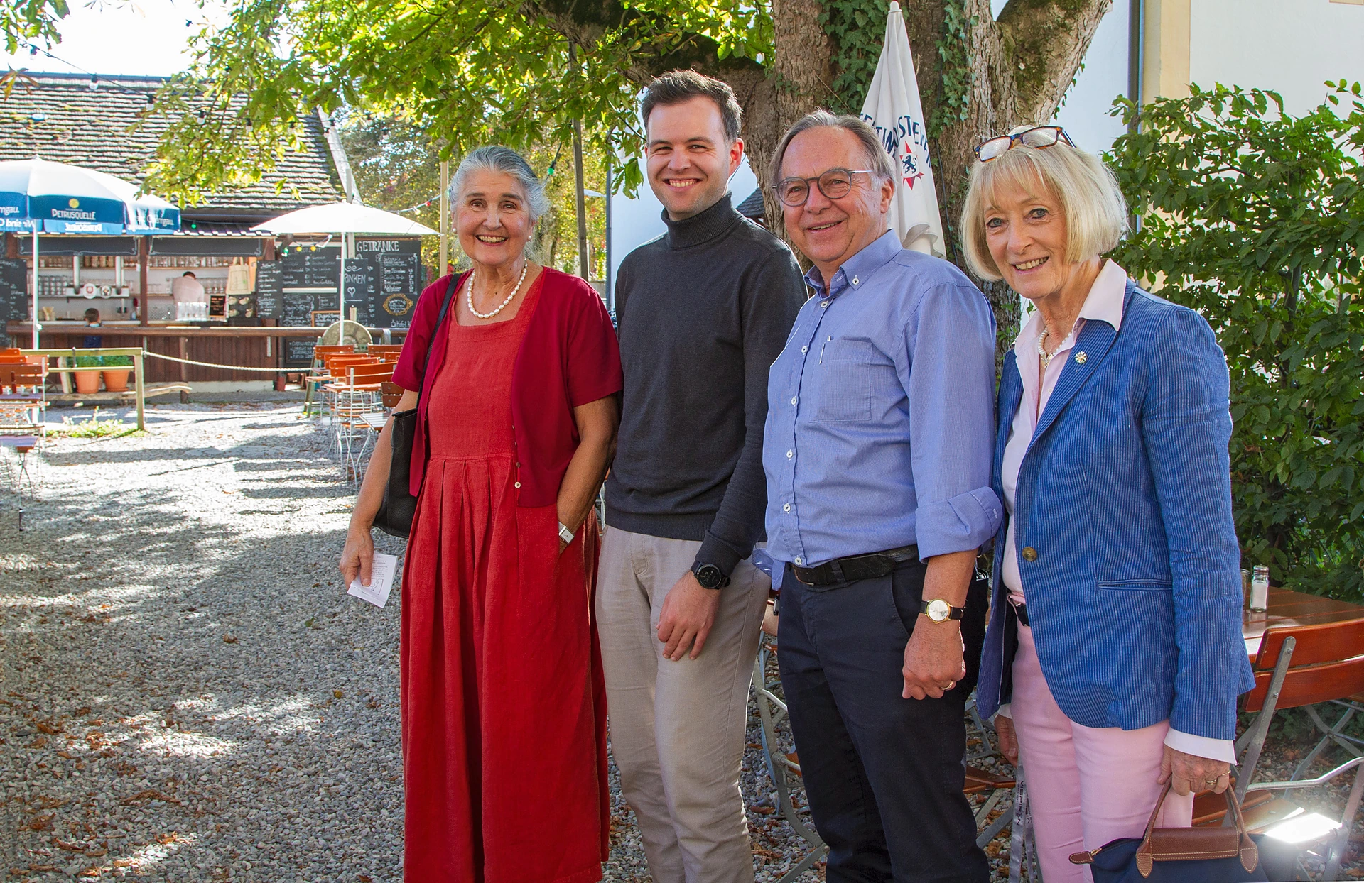 Vier Personen stehen lächelnd nebeneinander im Biergarten unter einem Kastanienbaum: Ursula Hauer in rotem Kleid, der Pianist Johannes Obermeier im dunklen Rollkragenpullover, Helmut Fietzek im blauen Hemd und Hanne Wittermann im blauen Blazer