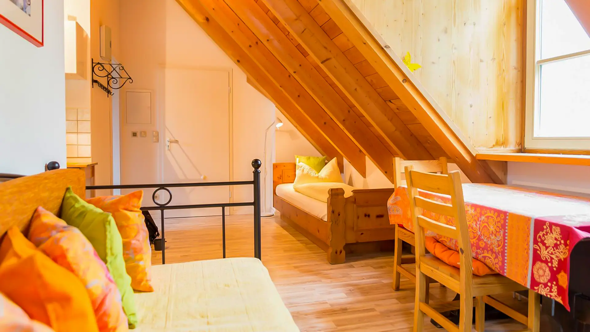 Apartment Schmetterling mit Couch, Schreibtisch und Bett unter der hölzernen Mansarde mit offener Balkenkonstruktion.