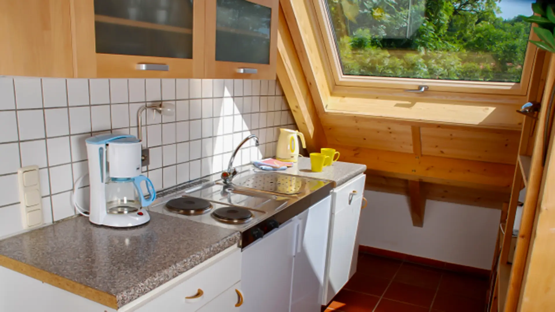 Thamm Ferienwohnung Ansicht der Küche in der Ferienwohnung Schmetterling mit Dachfenster, Küchenzeile, Waschbecken, weißen Fließen und Holzhängeschränken.