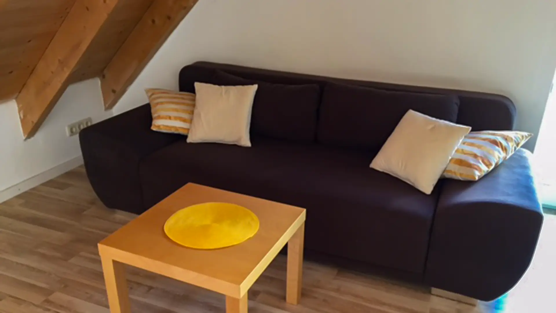 Thamm Ferienwohnung Sonnenblume - dunkelblaue Couch davor ein Holzsofatisch unter der Mansarde mit Holzfußboden.